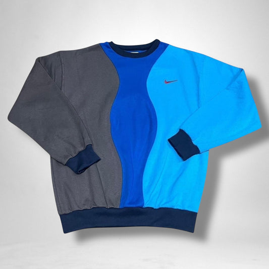 Reworked Nike jumper in blue and grey with vintage patchwork design, custom streetwear pullover laid flat on a neutral background